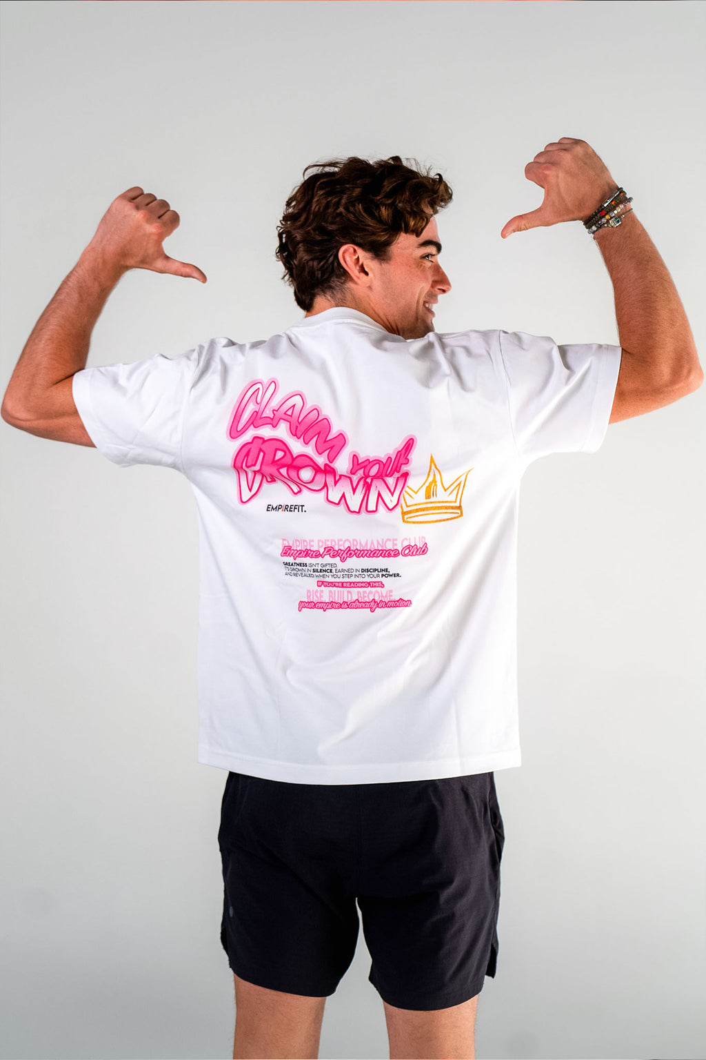 Male athlete pointing to the back graphic of the white Claim Your Crown Tee relaxed fit gym t-shirt by Empire Fit