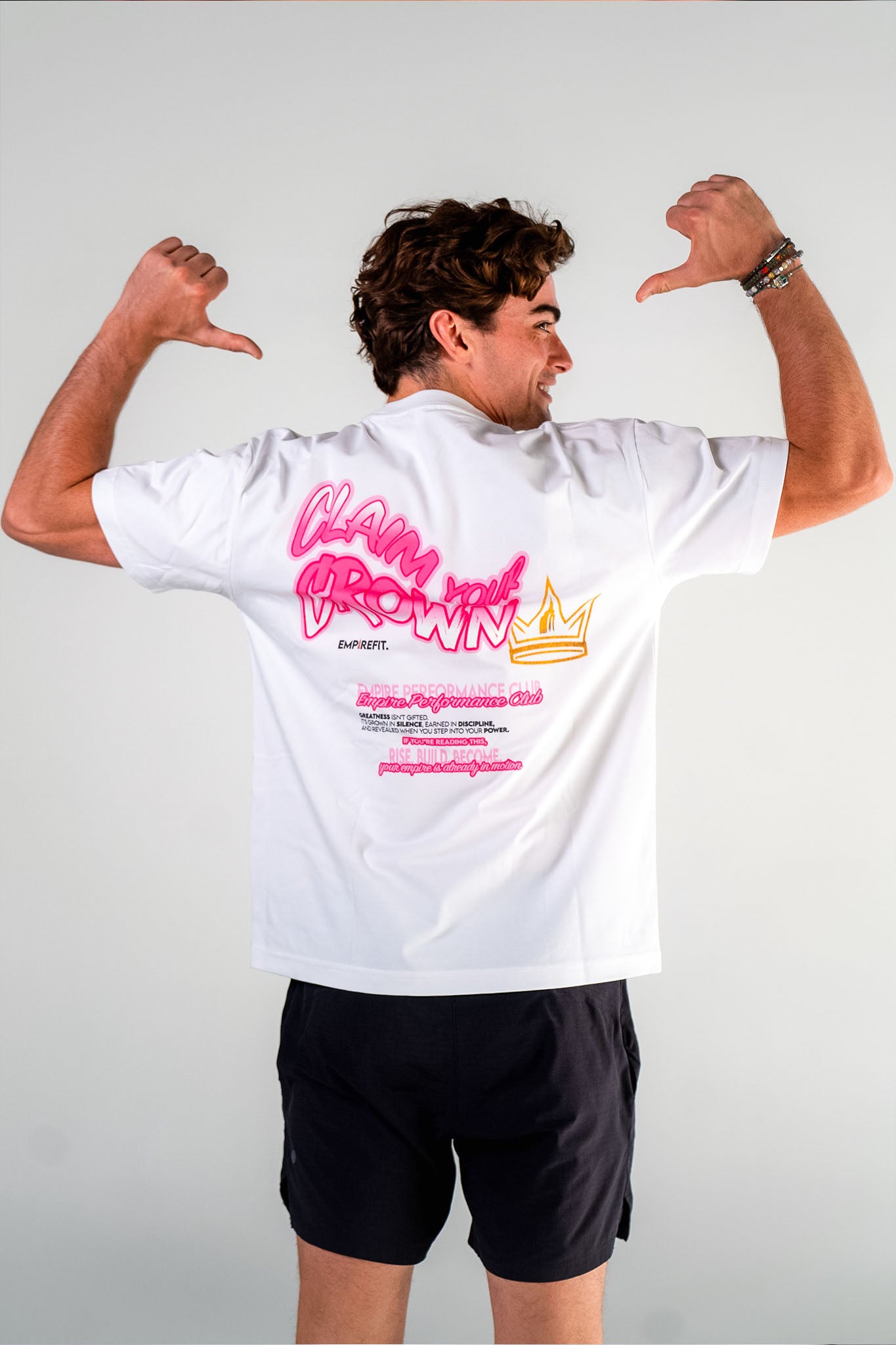 Male athlete pointing to the back graphic of the white Claim Your Crown Tee relaxed fit gym t-shirt by Empire Fit